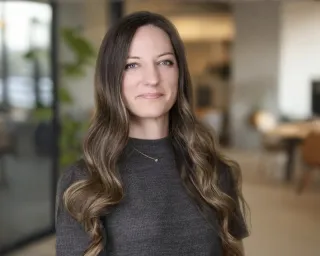 Professional woman in charcoal sweater smiling warmly in bright modern office with natural light